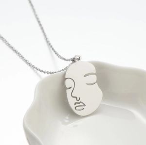 Abstract face line pendant necklace in silver finish on a minimalist white ceramic plate