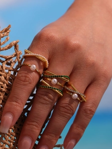 Detail of stacked gold-plated rings featuring white pearls and green zircon on hands