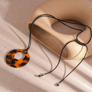 Macro detail of tortoiseshell resin pendant on minimal beige stone background with soft shadows