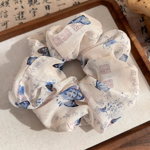 Detail of calligraphy print and blue butterfly pattern on a beige silk scrunchie