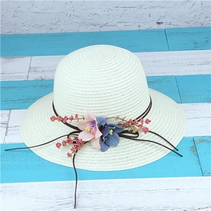 Dettaglio del cappello di paglia con finiture floreali colorate e accenti di bacche decorative