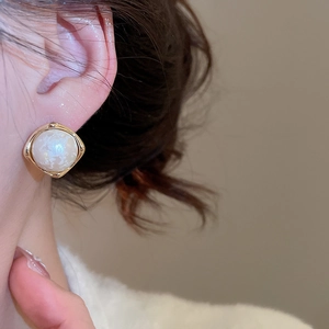 Close-up of gold geometric earrings with white pearl-texture stone on a model's ear