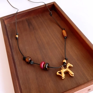 Détail du pendentif cheval doré avec perles œil de tigre et bois sur plateau