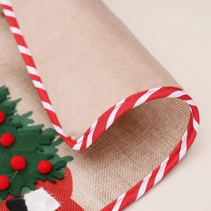 Burlap Christmas table runner featuring green tree pattern and red pom poms with striped edges