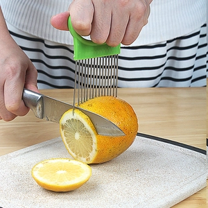 Stainless steel onion holder with green handle used for slicing oranges on a cutting board