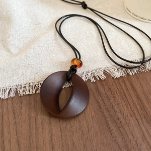 Detailed macro view of dark brown resin circle pendant and amber bead on wax cord necklace