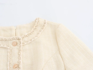 Dettaglio giacca in tweed beige con trama intrecciata, frange e bottoni in metallo oro