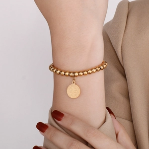 Dettaglio del bracciale con perline dorate e ciondolo religioso di San Benedetto