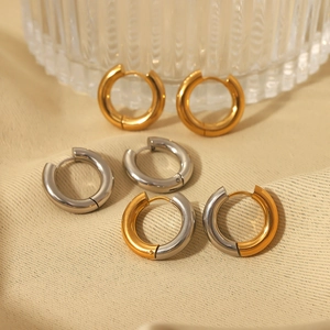 Three pairs of hoop earrings in gold and silver finish on a soft fabric texture