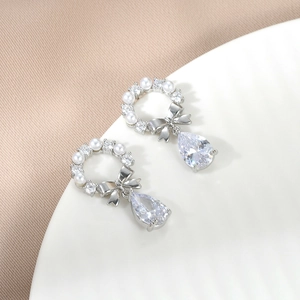 Detail of silver bow earrings featuring elegant white pearls and drop-shaped zircon stones