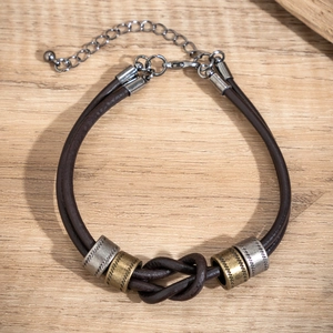 Dettaglio del bracciale in pelle marrone scuro con anelli in metallo e nodi su legno