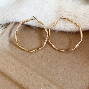 Macro shot of large golden hoop earrings with irregular hammered texture on fabric