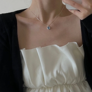 Detail of an oval light blue moonstone pendant necklace worn on a silver snake chain