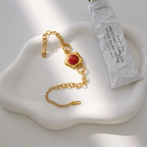 Detail of gold stainless steel bracelet with red agate stone on white ceramic tray