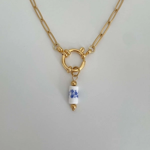 Detail of a gold necklace featuring a white cylindrical pendant with blue floral patterns