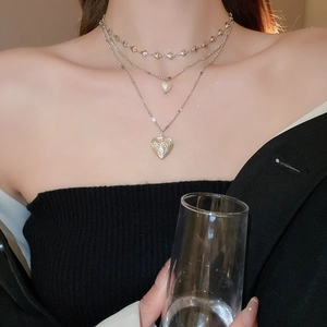 Detail of silver triple-layer necklace featuring heart charms and a white pearl pendant
