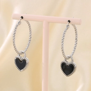 Détail de créoles torsadées argentées avec pendentifs en forme de cœur noir émaillé