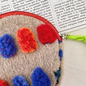 Detail of oatmeal plush round pouch with colorful crochet pom poms and green lanyard