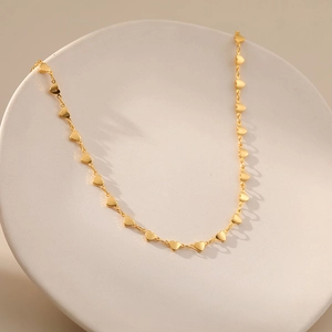 Detail of 18K gold plated heart chain necklace on white ceramic display plate
