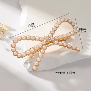 Elegant gold bow hair clip with white pearls and rhinestones on stone background