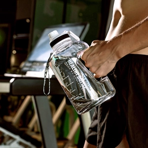 Close-up of a large sports water bottle with time markings held in a gym setting