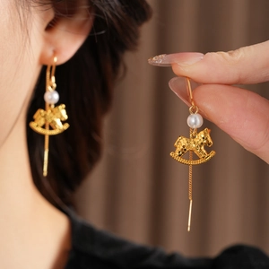 Detail of golden rocking horse earrings with pearls and elegant long wire design