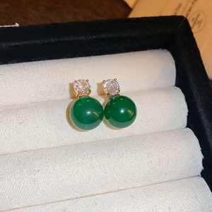 Detail of green sphere stud earrings with white zircon on beige velvet jewelry box