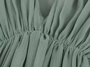 Detailansicht eines salbeigrünen Chiffonkleides mit feinen Falten und Stofftextur