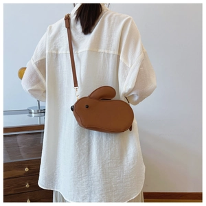 Gros plan d'un sac bandoulière lapin en cuir PU marron porté par un mannequin en blanc