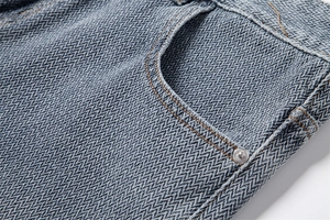 Detailed macro view of herringbone denim fabric with yellow stitching and metal rivet