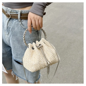 Detail of beige straw bucket bag with silver metal ring handle and fringe accents