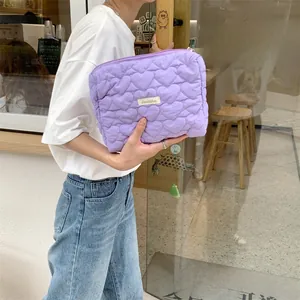 Close-up of a purple quilted heart cosmetic bag held by a model in a natural setting