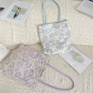 Detail of floral lace embroidery and logo label on pastel canvas tote bag with long straps
