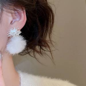 Close-up of snowflake stud earrings with white faux fur pom poms on model ear