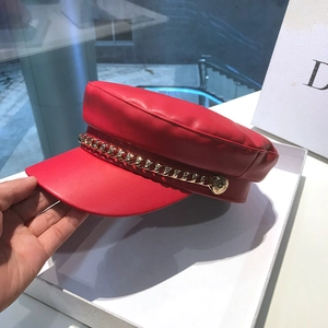 Red faux leather sailor cap with gold chain accent resting on a white gift box