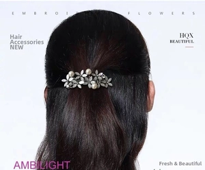 Detailed view of silver flower hair clip with pearls and rhinestones on dark hair