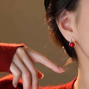 Macro view of gourd stud earrings with red beads and bow detail on a female model