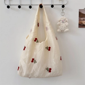 Detail of red cherry embroidery on a cream mesh tote bag with a soft sheep pendant