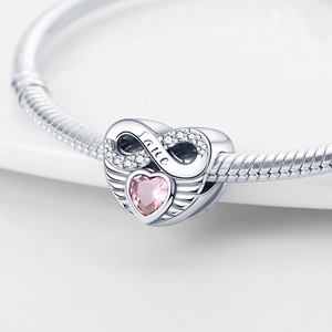 Macro shot of silver winged heart charm with pink crystal and Love infinity symbol