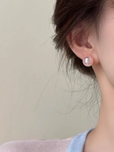 Close-up of small pink mermaid pearl stud earrings on ear with iridescent finish