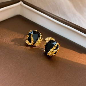 Gros plan de boucles d'oreilles dorées en forme d'épi avec une pierre précieuse noire facettée