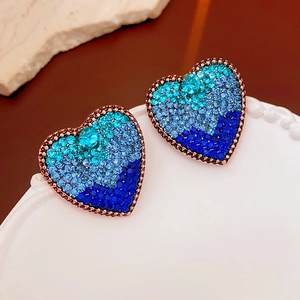 Macro detail of vintage heart stud earrings with blue gradient crystals on bronze base