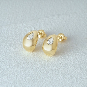Detailed close-up of golden teardrop stud earrings with clear zircon stones on white texture