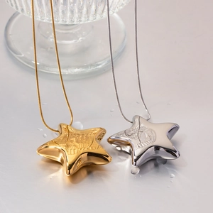 Polished 18K gold and silver star pendant necklaces with snake chains on a wet surface
