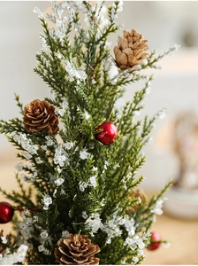 Close-up of frosted pine needles, red berries, and natural pine cones on a mini desk tree