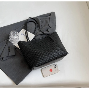 Top-down view of black woven tote bag styled with a grey blazer and accessories