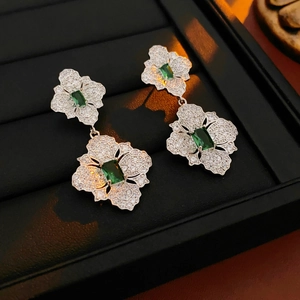 Detailed macro of floral silver earrings with sparkling zircon and green emerald centers