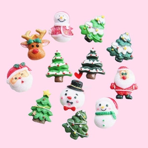 Flat lay of resin Christmas charms including Santa, snowmen and trees on pink background