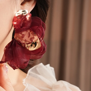 Detailed close-up of wine red fabric flower earring with irregular golden metal detail