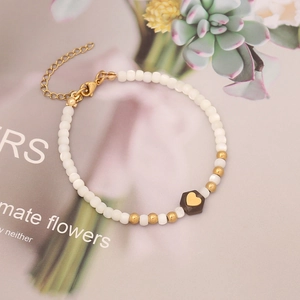Elegant beaded bracelet with white pearls and gold heart charm on a decorative background